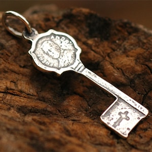 Peut inclure: Breloque en forme de clé en argent avec un design détaillé représentant un visage et le mot "ANDREAS" en haut. Le bas de la clé comporte une croix et le mot "PATIENCE".