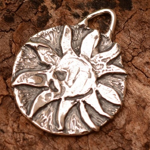 May include: A silver pendant in the shape of a sun with a textured surface.