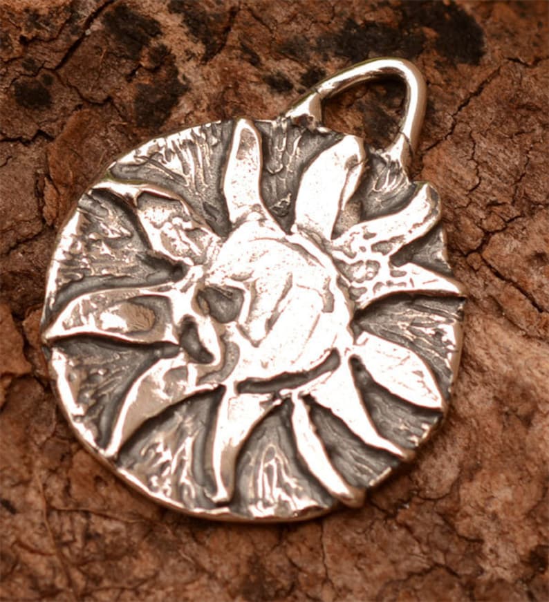 May include: A silver pendant in the shape of a sun with a textured surface.