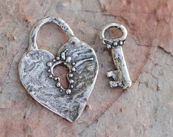 May include: A silver heart-shaped padlock with a keyhole in the shape of a key. The padlock and key are both textured and have a rustic look.