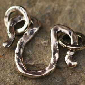 May include: Silver-toned metal clasp with a textured, hammered finish. The clasp is shaped like a snake with a looped tail.