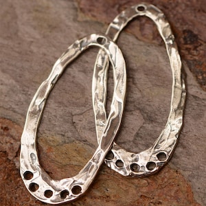 May include: Two silver oval-shaped metal pieces with a hammered texture and multiple holes. The pieces are stacked on top of each other.