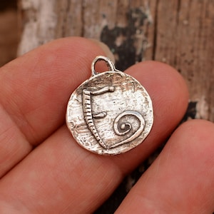 May include: Silver charm with a textured surface and a stylized letter 'E' and a spiral design.