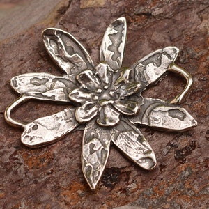 May include: A silver flower charm with a textured surface and a loop for attaching to jewellery.