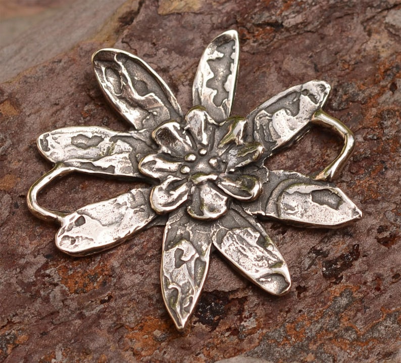 May include: A silver flower charm with a textured surface and a loop for attaching to jewellery.