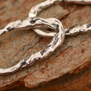 May include: Two silver rings linked together, each ring has a textured, hammered finish.