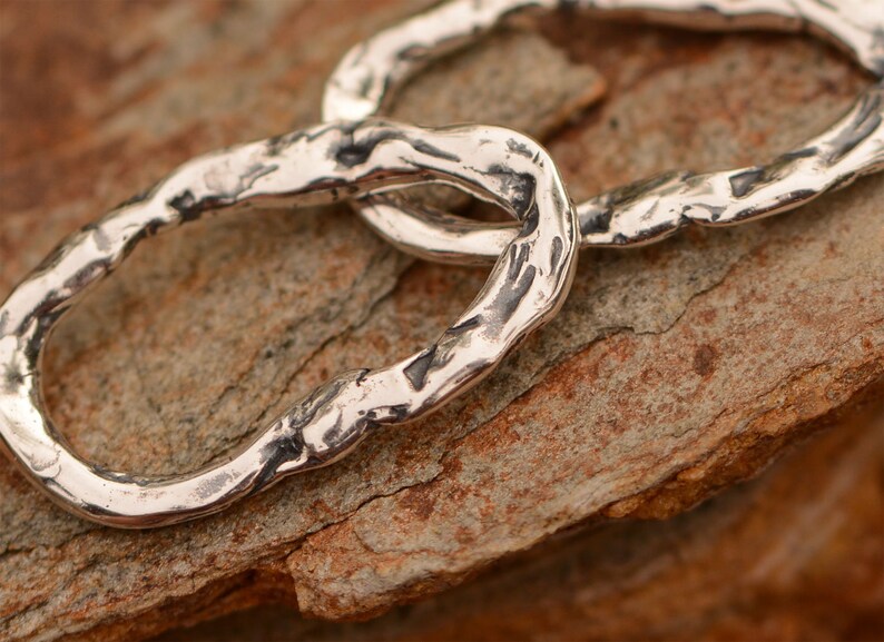 May include: Two silver rings linked together, each ring has a textured, hammered finish.
