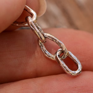 May include: Close-up of a silver chain with a textured finish. The chain is made of interlocking oval links.