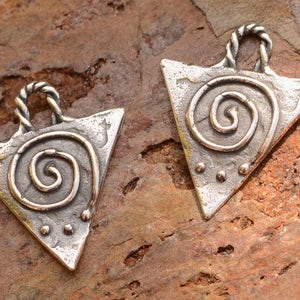 May include: Two silver triangle pendants with a spiral design and three small dots. The pendants have a loop at the top for hanging.
