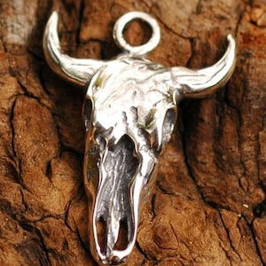 May include: Silver pendant in the shape of a bull skull with a loop at the top for attaching a chain.