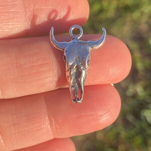 May include: Silver bull skull charm pendant with a loop at the top for attaching to a necklace or bracelet.