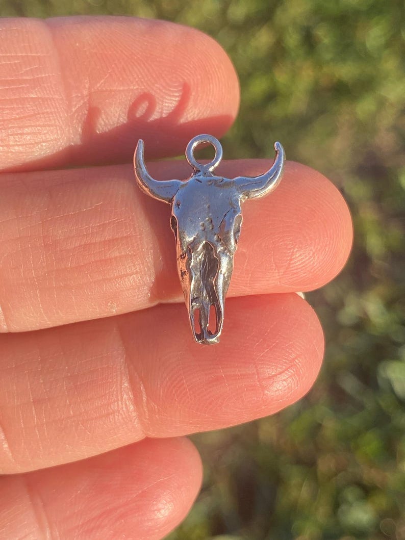 May include: Silver bull skull charm pendant with a loop at the top for attaching to a necklace or bracelet.