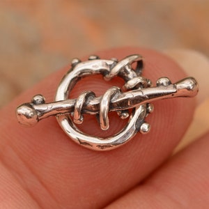 May include: Silver toggle clasp with a twisted wire design and a circular ring. The clasp has a rustic, handmade look.