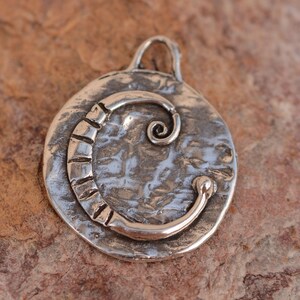 May include: A silver charm with a textured surface and a stylized letter C. The charm has a loop at the top for attaching to a necklace or bracelet.