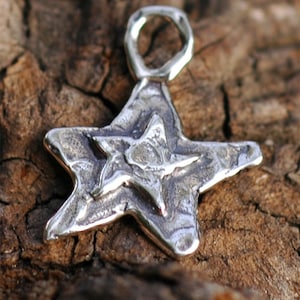May include: A silver charm in the shape of a five-pointed star with a textured surface. The star has a loop at the top for attaching to a necklace or bracelet.