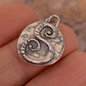 May include: Silver pendant with a hammered finish and a stylised letter 'S' design. The pendant has a loop at the top for attaching to a chain.
