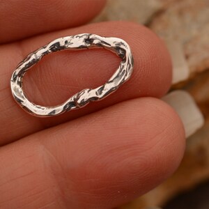 May include: A silver oval-shaped ring with a textured, organic design. The ring is made of metal and has a rough, uneven surface.