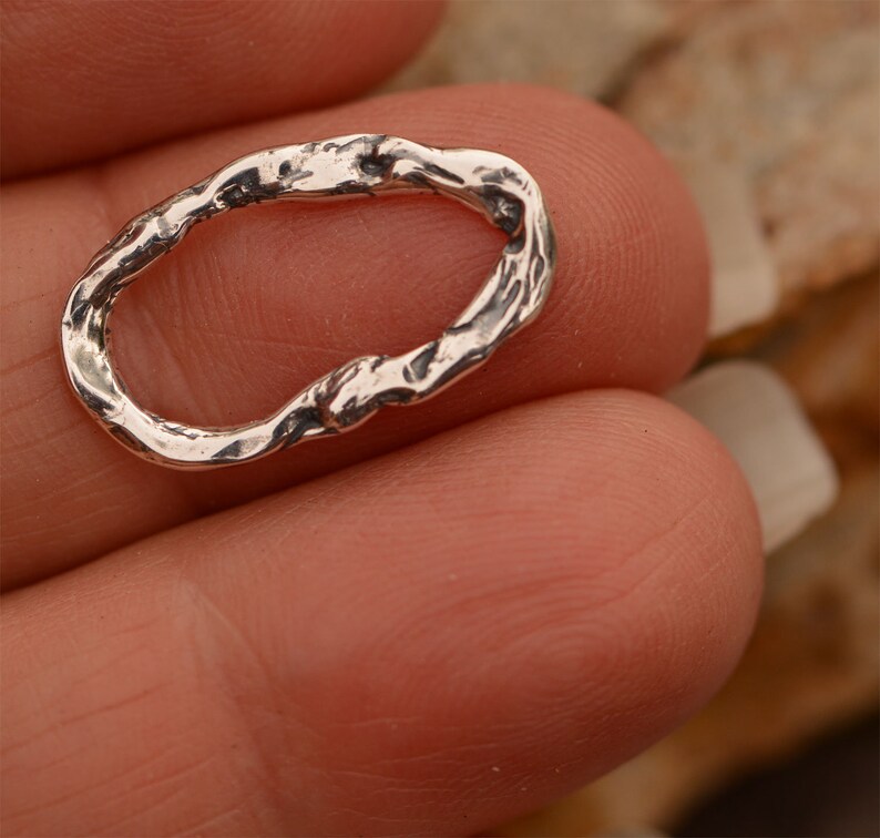 May include: A silver oval-shaped ring with a textured, organic design. The ring is made of metal and has a rough, uneven surface.