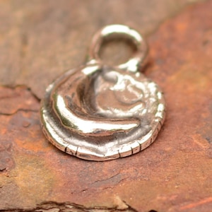 May include: A silver charm in the shape of a crescent moon with a textured surface. The charm has a loop at the top for attaching to a necklace or bracelet.