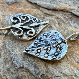 May include: Two silver leaf pendants with detailed designs. One has swirling patterns, the other a textured surface with small dots. Each has a loop for a chain. Ideal for jewellery making.