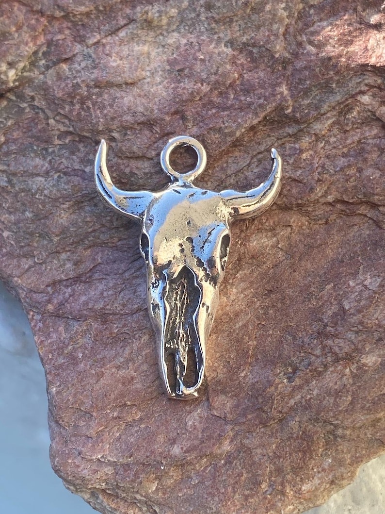 May include: Silver bull skull charm pendant with a loop at the top for attaching to a necklace or bracelet.
