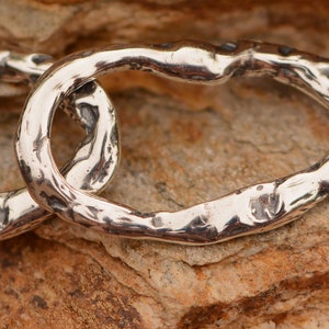 May include: Close-up of a silver chain with a textured, hammered finish. The chain is made of thick, oval links that are connected together.