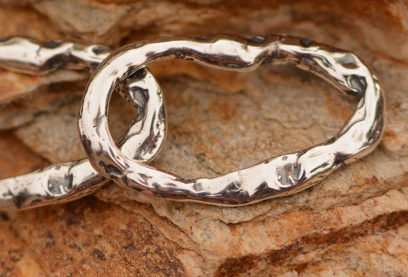 May include: Close-up of a silver chain with a textured, hammered finish. The chain is made of thick, oval links that are connected together.