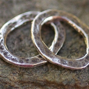 May include: Two silver rings with a hammered texture. The rings are interlocked and have a rustic, handmade look.