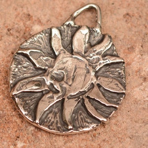 May include: A silver pendant in the shape of a sun with a textured surface.