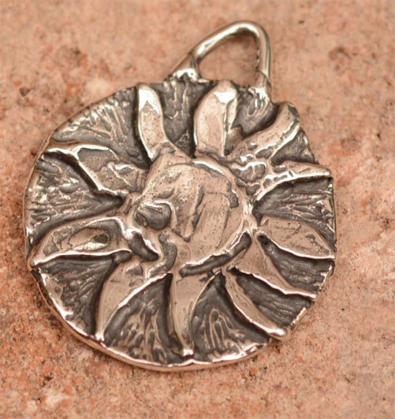 May include: A silver pendant in the shape of a sun with a textured surface.