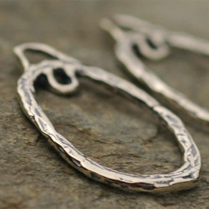 May include: A pair of silver hoop earrings with a hammered texture. The earrings are open and have a slightly irregular shape.