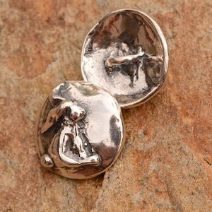 May include: A pair of silver-toned metal buttons featuring a rabbit design. The button on the left has a raised rabbit design, while the button on the right is plain.