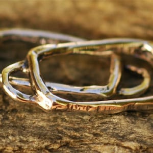 May include: Two silver metal rings, one inside the other, with a rough, textured finish. The rings are open on one side and have a rounded shape.