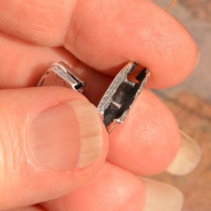 May include: Close-up of a silver-toned metal clasp with a textured surface. The clasp is open and shows the inner mechanism.