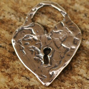 May include: A silver heart-shaped padlock charm with a keyhole in the center. The charm has a textured, hammered finish.