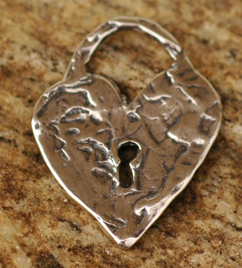 May include: A silver heart-shaped padlock charm with a keyhole in the center. The charm has a textured, hammered finish.