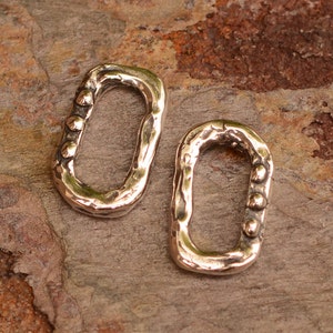 May include: Two silver oval-shaped jump rings with textured surfaces and small silver beads on one side.