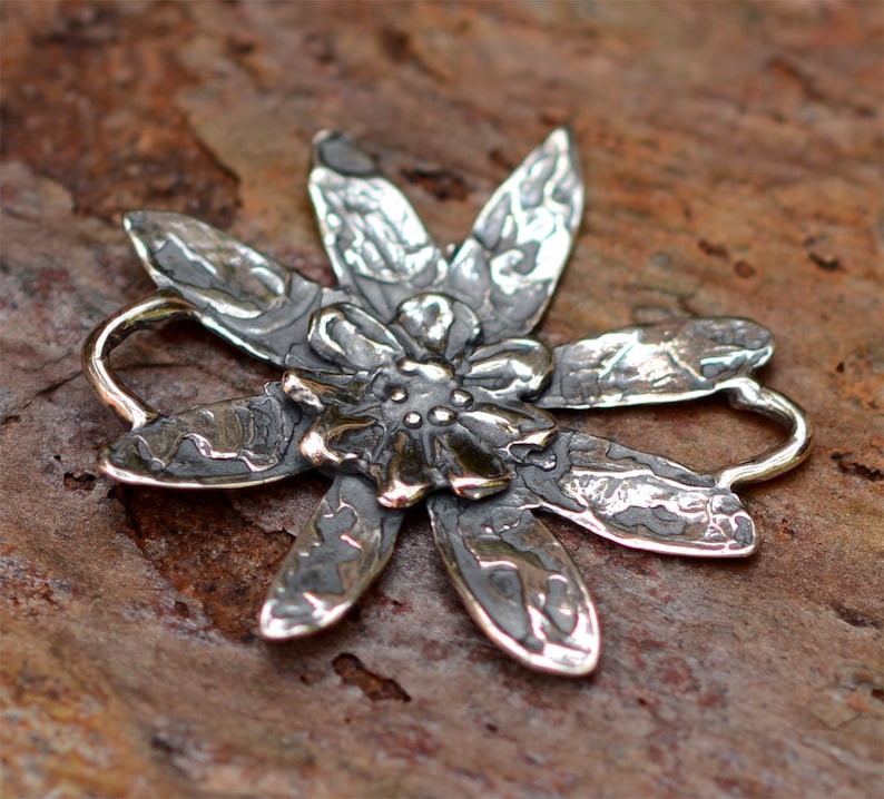 May include: A silver flower pendant with a textured surface and a raised centre. The pendant has a loop at the top for attaching to a chain.