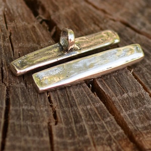 May include: Two silver rectangular metal pieces with a loop on one end. The pieces are laying on a wooden surface.
