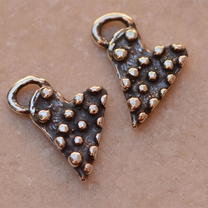 May include: Two silver heart-shaped charms with a textured surface and a loop at the top. The charms are covered in small, raised dots.