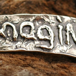 May include: A silver metal tag with the word "Imagine" embossed in a textured, rustic style. The tag has two holes on either side.