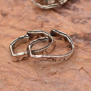 May include: Two silver rings with a textured finish, interlocked together. The rings are made of metal and have a hammered look.