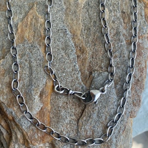May include: A silver chain necklace with a lobster clasp closure. The chain is made of oval links.