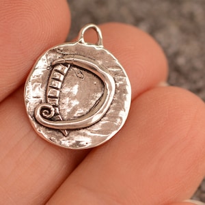 May include: A silver charm with a textured surface and a raised letter D. The charm has a loop at the top for attaching to a necklace or bracelet.