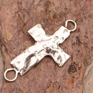 May include: Silver cross charm with a hammered texture and two jump rings for attaching to jewelry.