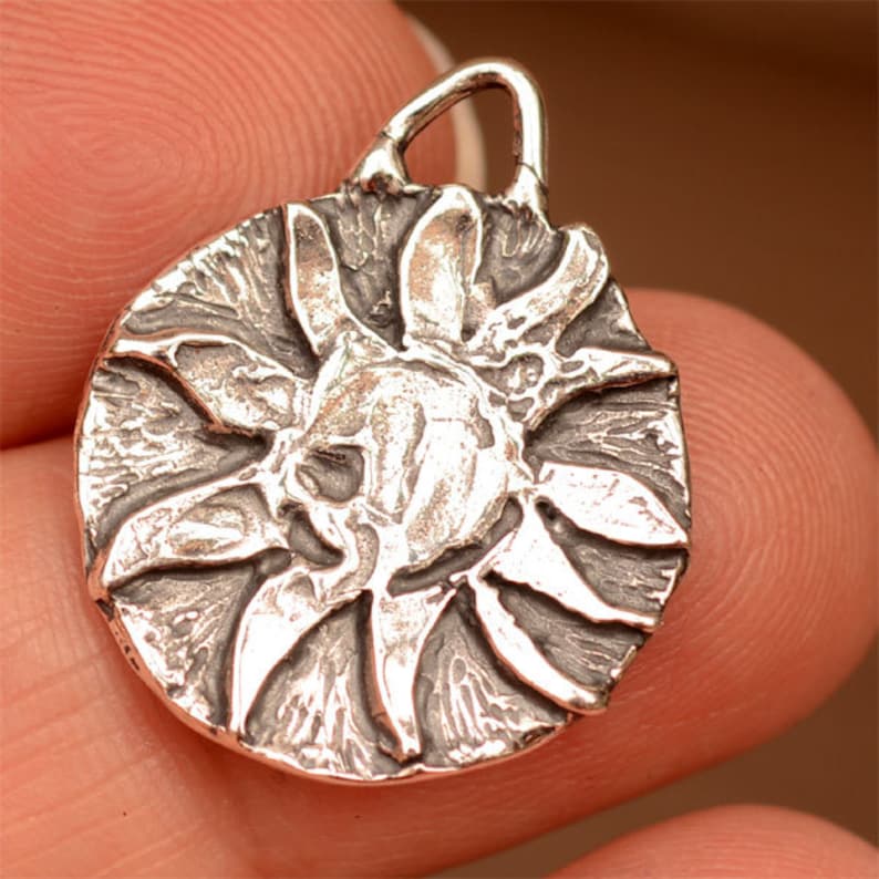 May include: A silver pendant charm featuring a detailed, textured design of a sun with rays.