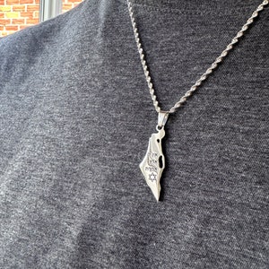 Può includere: Una collana con catena d'argento con un ciondolo a forma di contorno di Israele. Il ciondolo ha una scritta in ebraico, tra cui la parola "Israele" e una stella di David.