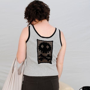 以下が含まれることがあります： 背中が黒のクロシェの骸骨のデザインのグレーのタンクトップ