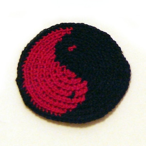 Puede incluir: Un símbolo yin yang tejido a crochet con un diseño rojo y negro.
