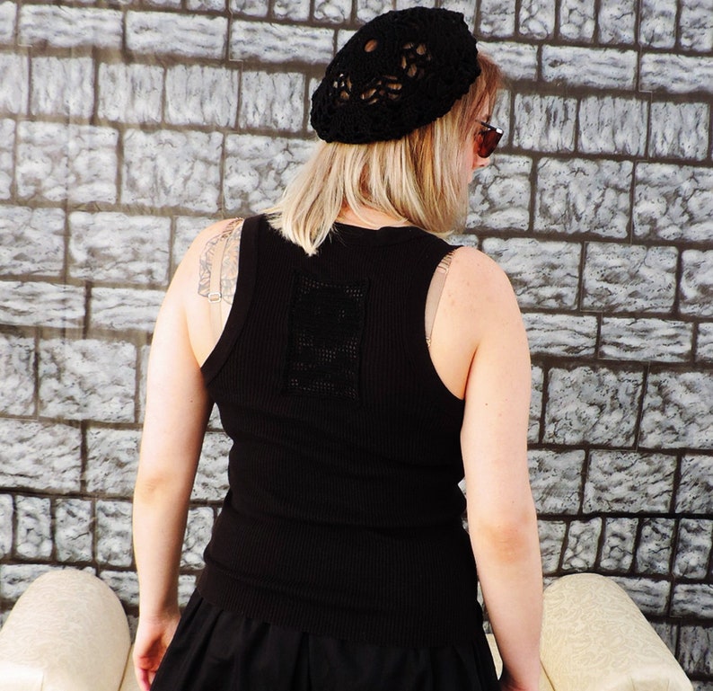 May include: A black sleeveless tank top with a crocheted design on the back. The tank top is made of a ribbed fabric and has a scoop neck.